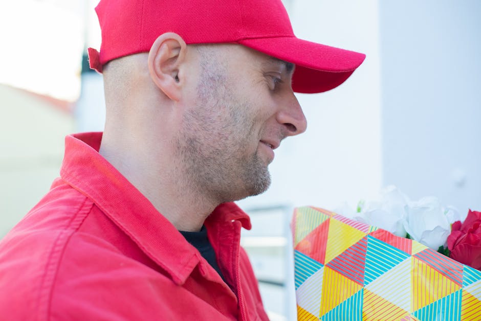 A delivery person wearing a red cap and red jacket is seen holding a floral gift wrapped in colorful geometric-patterned paper, with visible white and red flowers partially peeking out. The scene is s
