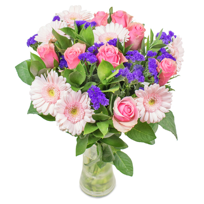 Elegantly staged in a clear glass vase, this stunning bouquet stands as a fresh ode to Motspur Park's family gardens and tree-lined roads. About eight pink roses-ranging from tightly wrapped buds to half-unfurled blooms-are the stars of this arrangement, their classic spiral petals exuding subtle romance. These are gracefully complemented by roughly six pale pink gerbera daisies, each with broad, round faces and lighter, almost luminescent centres. Intermixed throughout are vivid purple statice clusters, lending dramatic depth and a contemporary touch of texture. The robust green foliage at the base is reminiscent of the lush canopies surrounding Beverley Park, reinforcing the bouquet's freshness and vitality. Layers of petals and greenery are clearly visible through the vase, adding to the transparency and natural appeal. Filtered sunlight brings out a gentle glow in the daisy and rose petals, creating a serene yet lively composition. Designed to be a delightful gesture for birthdays, anniversaries, or as a sophisticated splash of colour for any space, this arrangement is perfect for same-day delivery across Motspur Park and West Barnes. The mood is cheerful, affectionate, and quietly celebratory-every stem reflecting the thoughtful expertise of Motspur Park Florist.