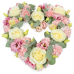 A tender, heart-shaped floral tribute dominates the image, its edges and centre completely defined by a carefully blended mix of pastel flowers and muted greenery. Creamy yellow and ivory roses are scattered throughout the heart, each bloom fully formed with velvety, layered petals that curl outwards in classic, elegant spirals. Between and around these roses, soft pink carnations create a rich, ruffled texture, their countless petals overlapping like fine fabric, giving the wreath a comforting, cushioned look. Deeper pink and mauve lisianthus blossoms are woven among the lighter tones, their more open, trumpet-like forms and slightly darker centres introducing depth, like gentle shadows cast along the quiet streets near Motspur Park. Cool, silvery-green eucalyptus leaves thread through the design, their rounded shapes and subtle sheen providing a calming contrast and outlining the heart with natural grace. Little yellow-green buds peek through the petals, suggesting fresh beginnings and the enduring continuity of love even in times of parting. All of this is set against a pristine white background, which allows the colours and textures to be clearly seen and appreciated. The mood carried by the arrangement is peaceful and compassionate, making it a fitting choice for a funeral, remembrance service, or condolence gesture delivered to families in Motspur Park and the surrounding community. The wreath feels like a heartfelt message in floral form, created by a local florist who understands how important it is to offer comfort, solace, and beauty when someone precious has been lost.